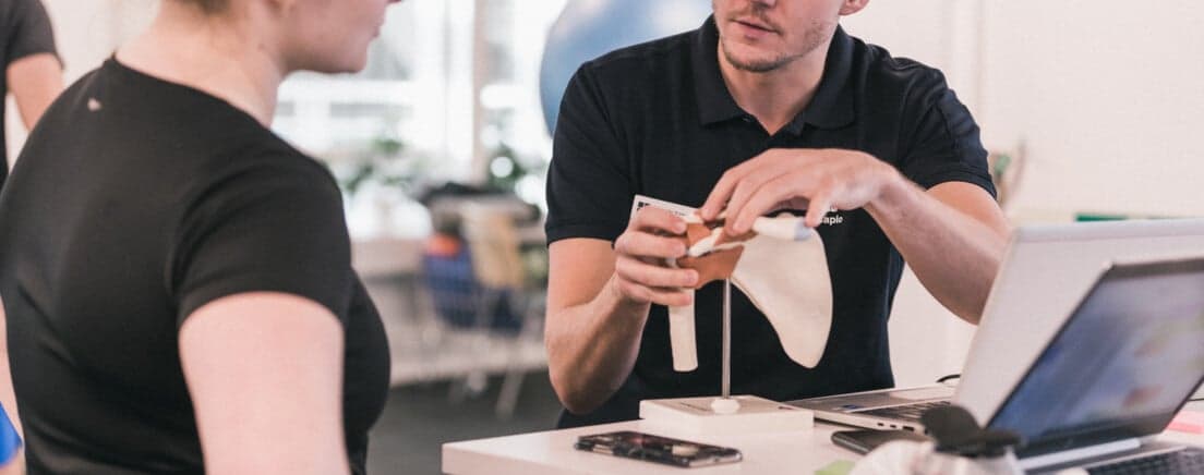 Fysioterapeut visar patienten hur axeln ser ut på en axelmodell
