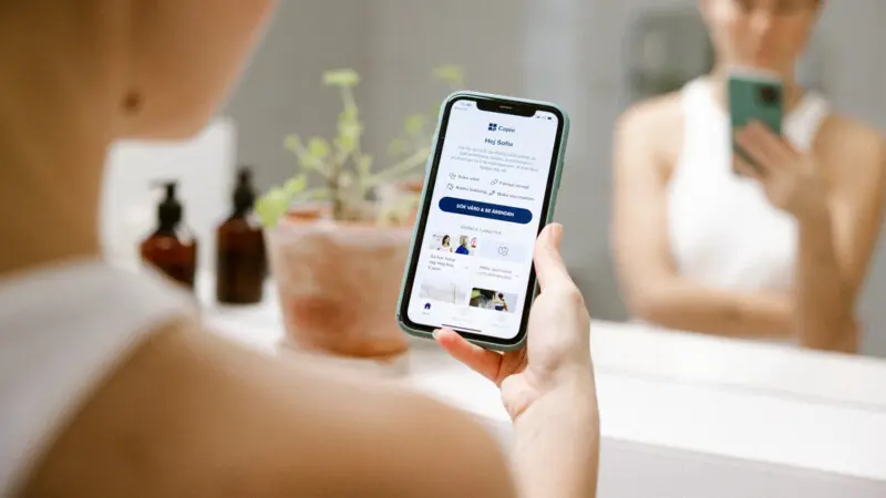 Medarbetare håller i en mobil och visar Capios app Medarbetare håller i en mobil och visar Capios app
