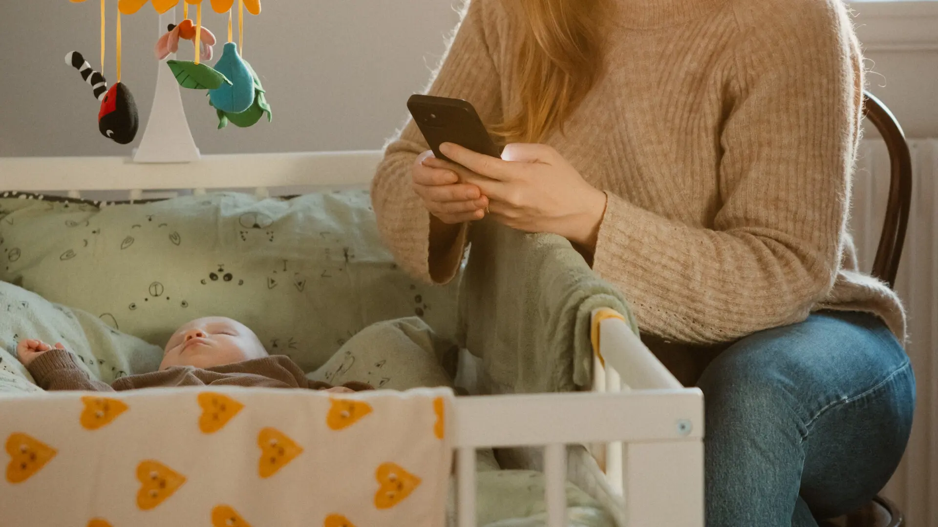 Mamma som sitter vid sin bebis och använder sin telefon