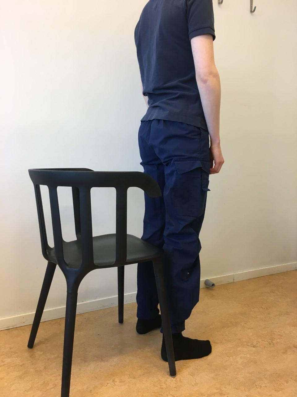 Person st&aring;r rak med ryggen &aring;t en stol. 