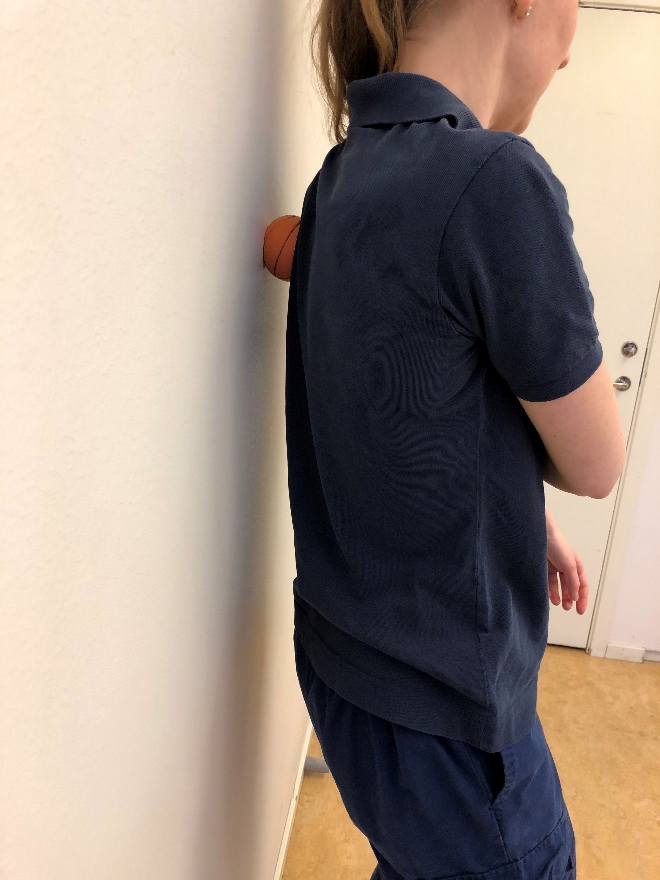 Tjej lutar sig mot v&auml;gg med bollen mellan p&aring; sm&auml;rtande omr&aring;det.