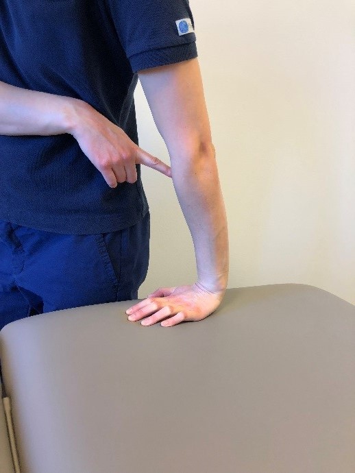 Person st&aring;r bredvid brits med ena handflatan tryckt mot underlaget. Amen t&ouml;js n&aring;got fram&aring;t. 