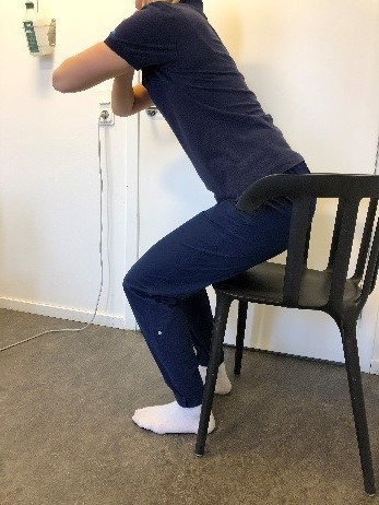 Person som halvt reser sig från en stol. Armarna i kors framför bröstet.