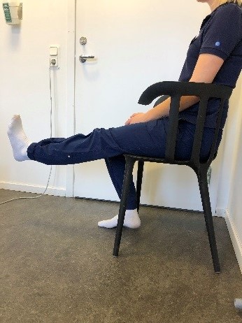 Person sitter på stol. Ena foten platt mot golvet, andra benet är utsträckt.