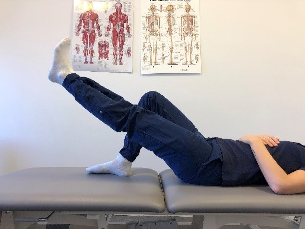 Person ligger på brits med armarna avslappat över magen. Ena knät är böjt och foten vilar platt mot underlaget, det andra benet är utsträckt en bit upp i luften.