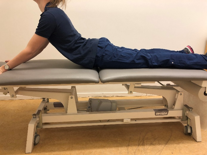 Person liggandes p&aring; mage p&aring; en brits med huvudet och &ouml;verkoppen lyft upp&aring;t med hj&auml;lpa av n&auml;stan raka fram&aring;tstr&auml;ckta armar. 