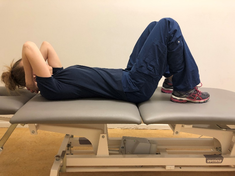 Tjej liggandes p&aring; rygg p&aring; en brits med uppdragna f&ouml;tter och h&auml;nderna bakom nacken.