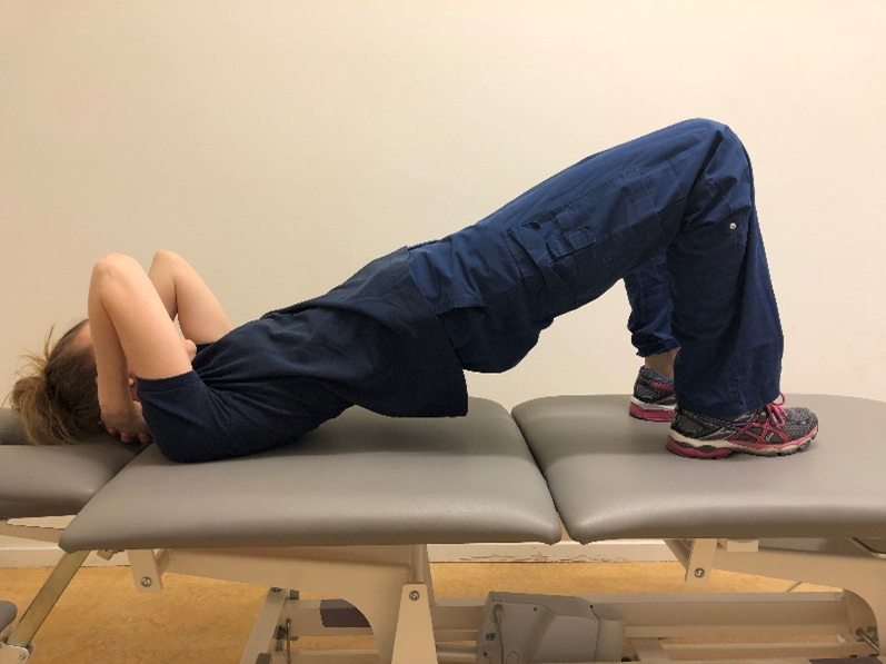 Tjej liggandes p&aring; rygg p&aring; brits med f&ouml;tterna uppdragna och underkroppen lyft upp&aring;t. 